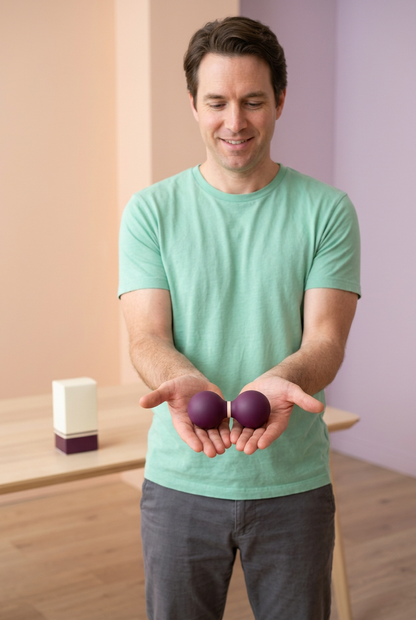 Adult Western male model holding the same single plum and cream peanut-shaped massage accessory